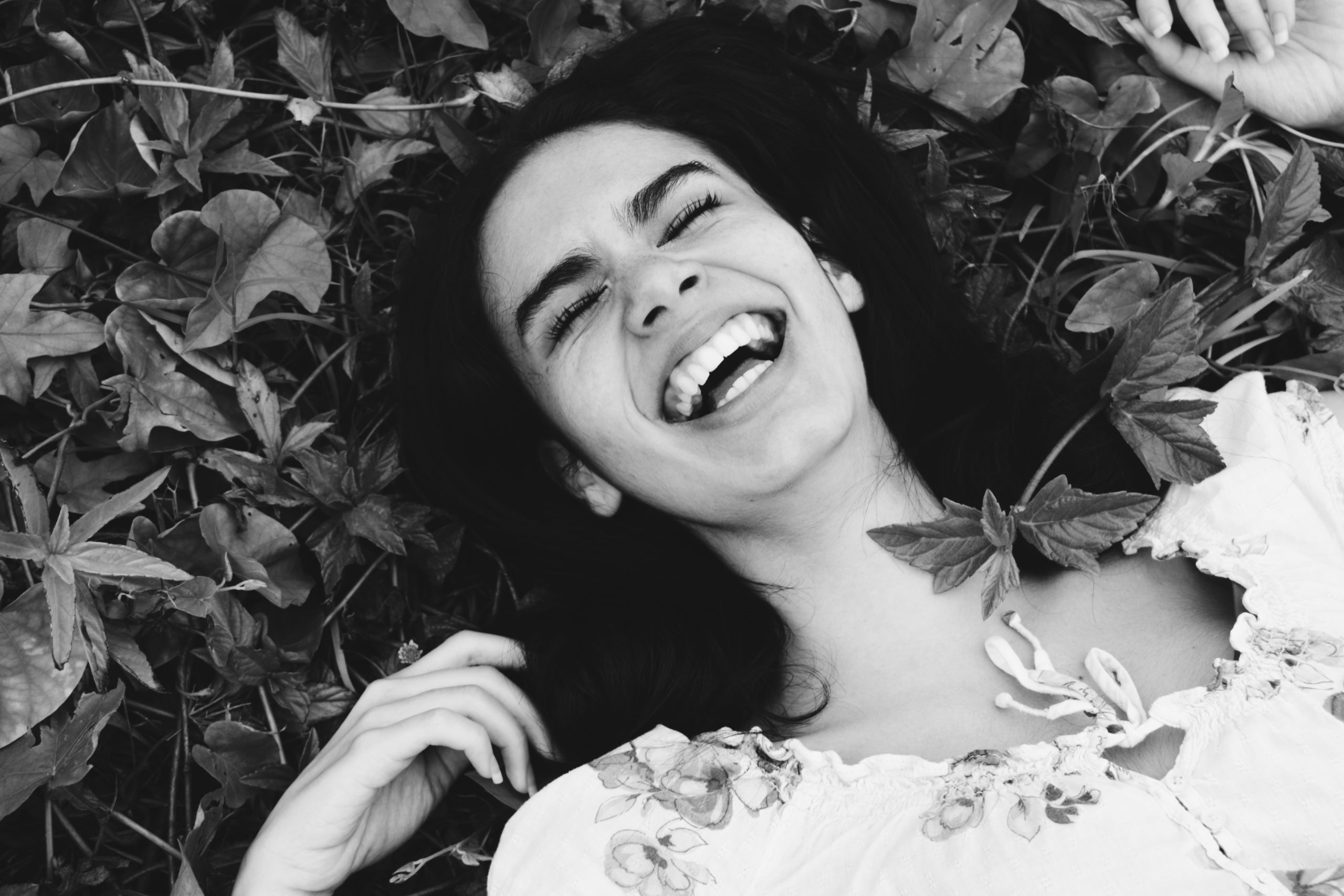 A greyscale image of a woman laughing as she lays on the ground.
