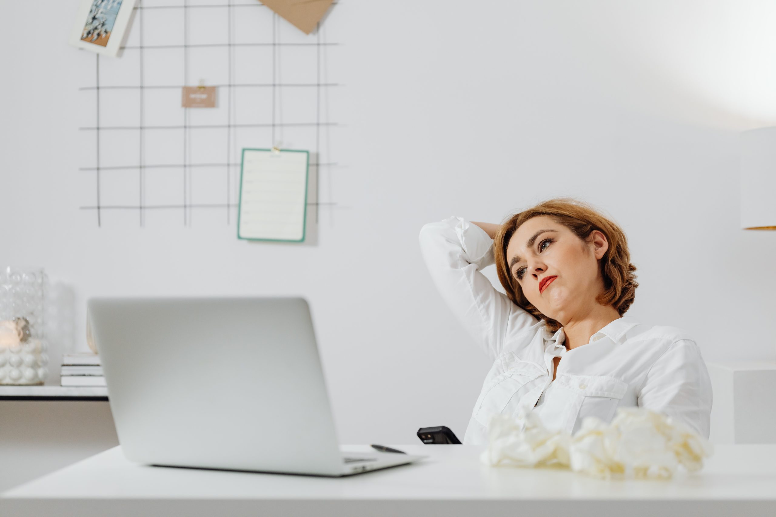 A woman sitting at a desk, leaning backwards, looking tired.