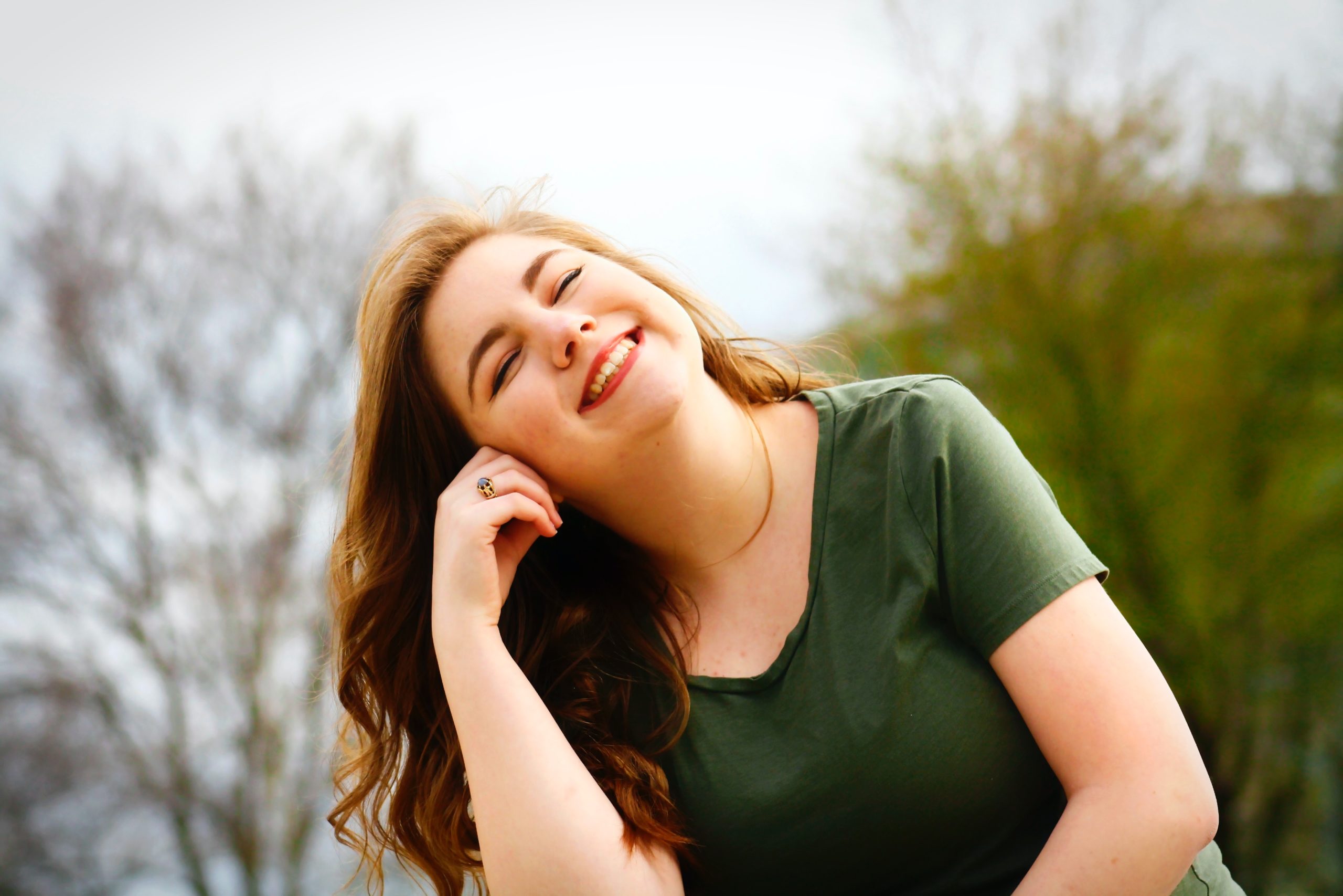 A smiling woman sitting outside, leaning her head on her hand.