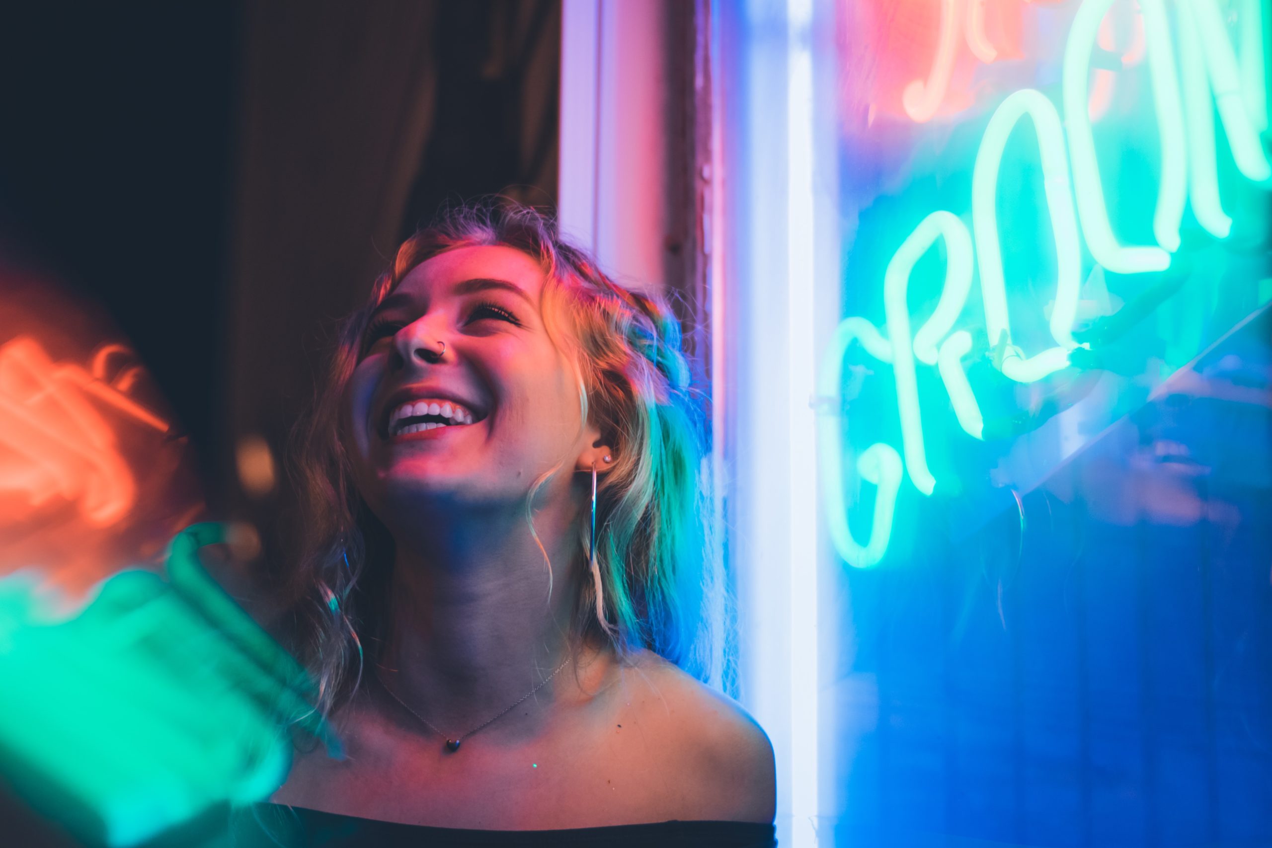 A woman smiling in the light of some neon shop signs.