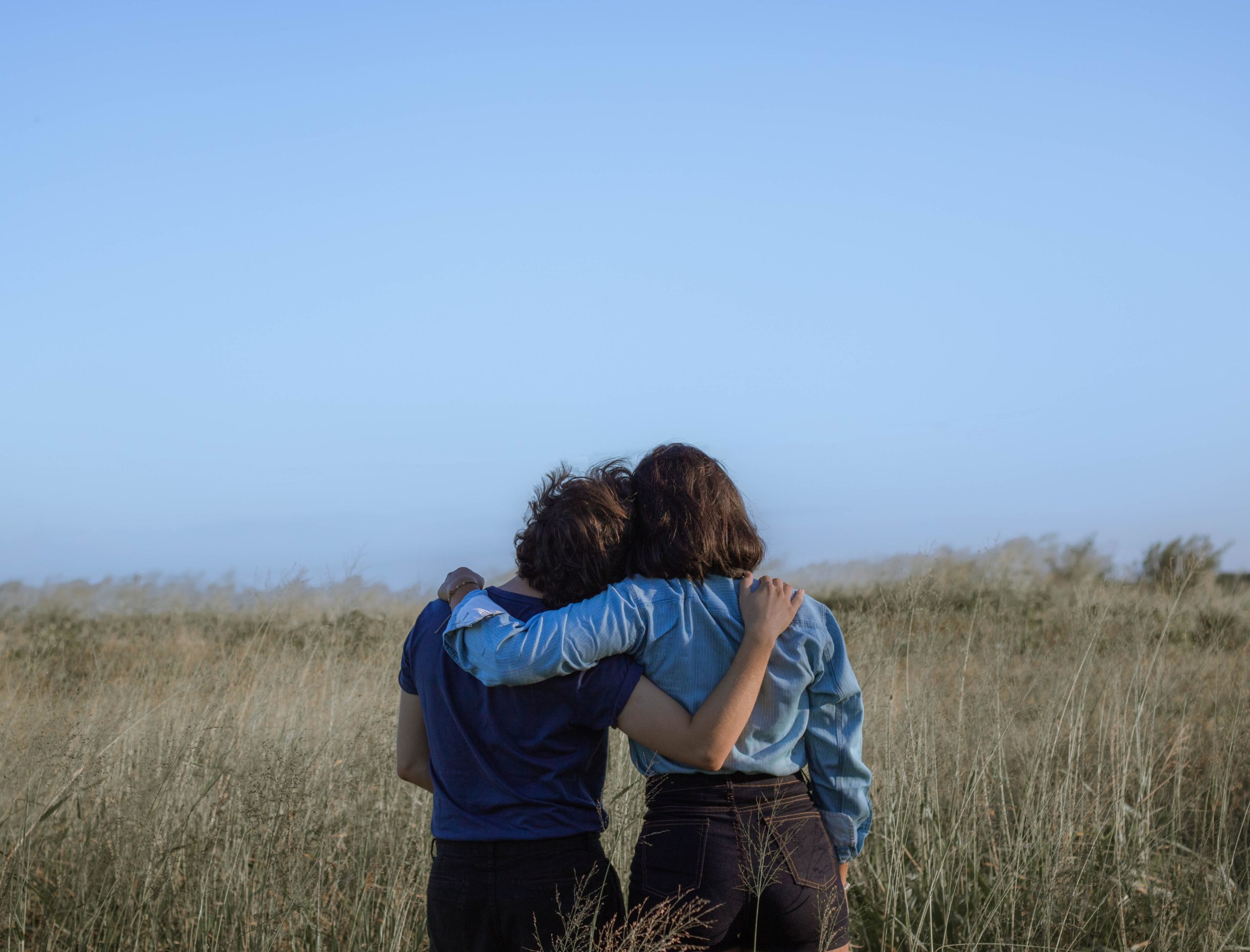 Two people standing in a field, an arm around each other.