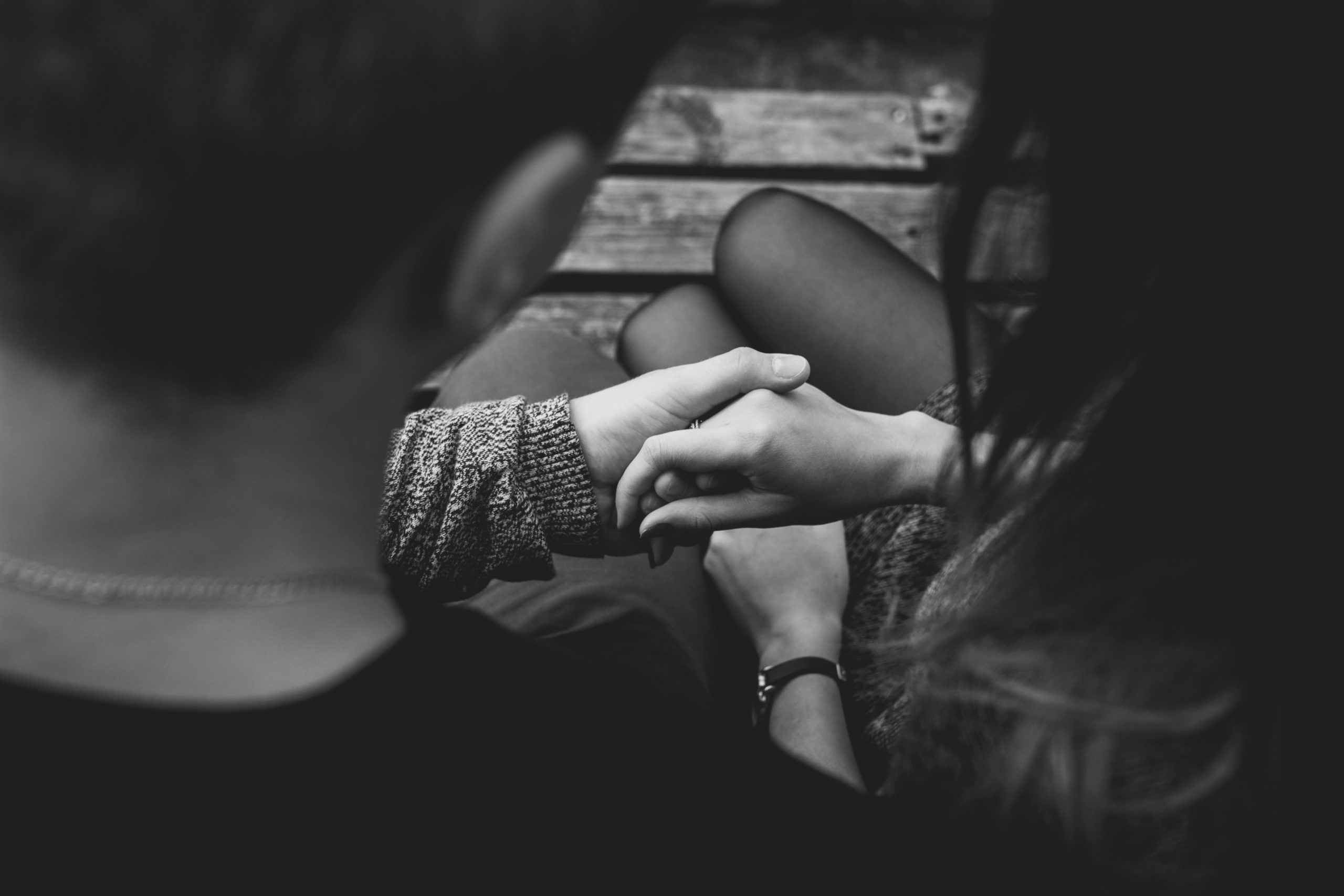 A greyscale image from behind a couple's shoulders, between which they're holding each other's hand.