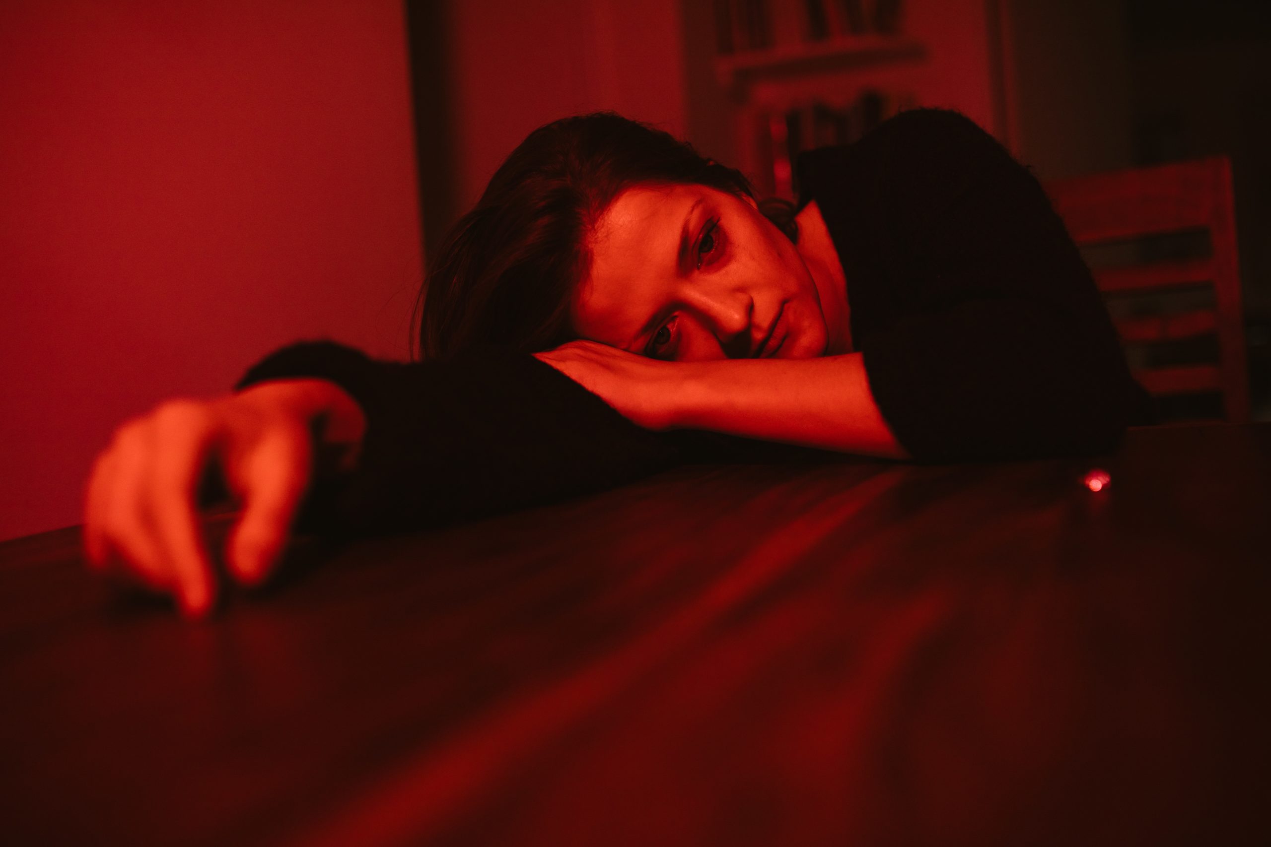 A red-lit image of a woman, crying, laying on her arm on a table.