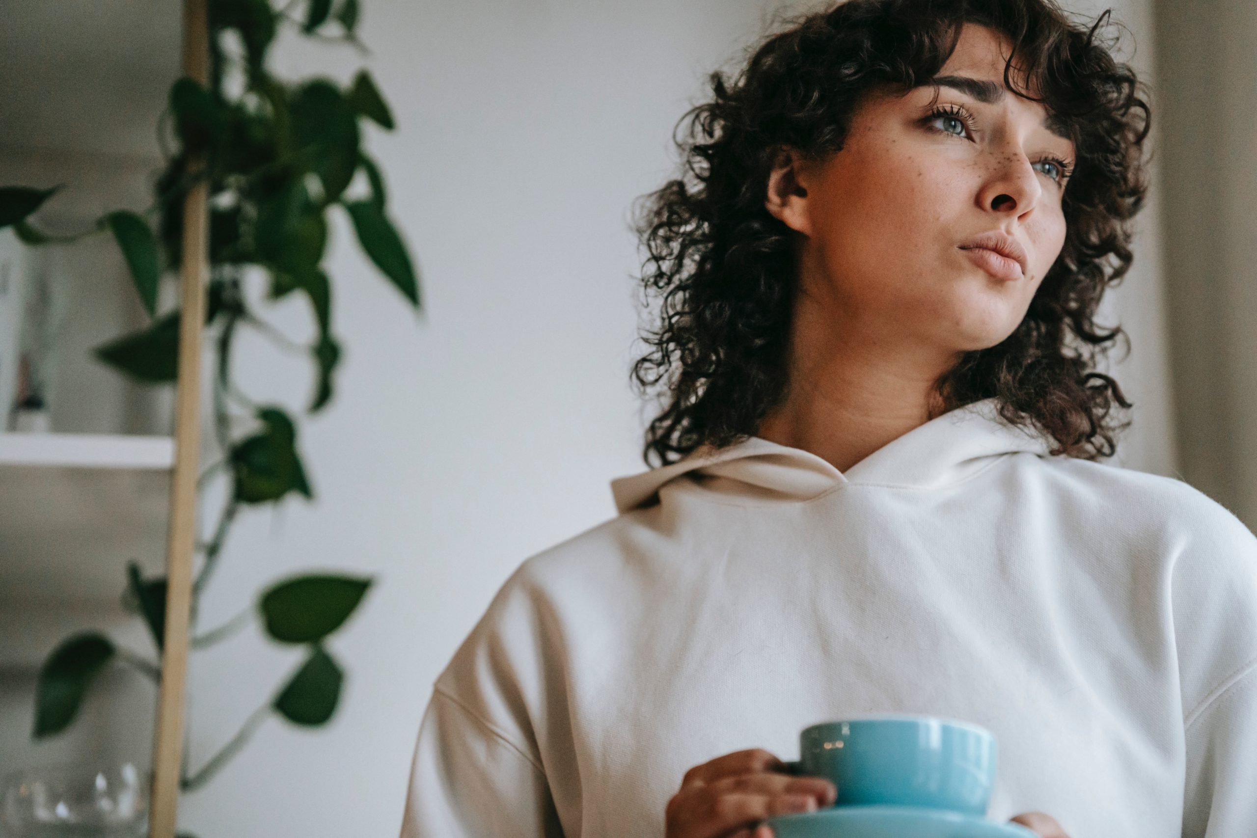 A woman looking pensive as she holds a mug of tea.