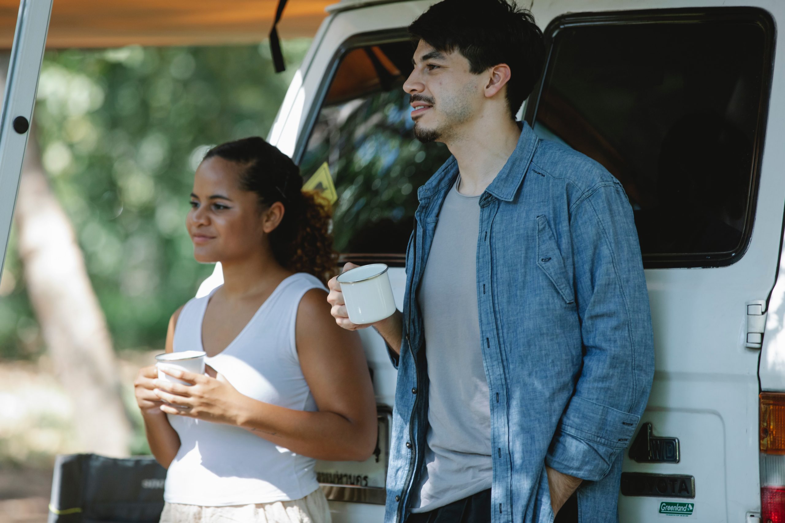 Two people drinking coffee outside of a van.
