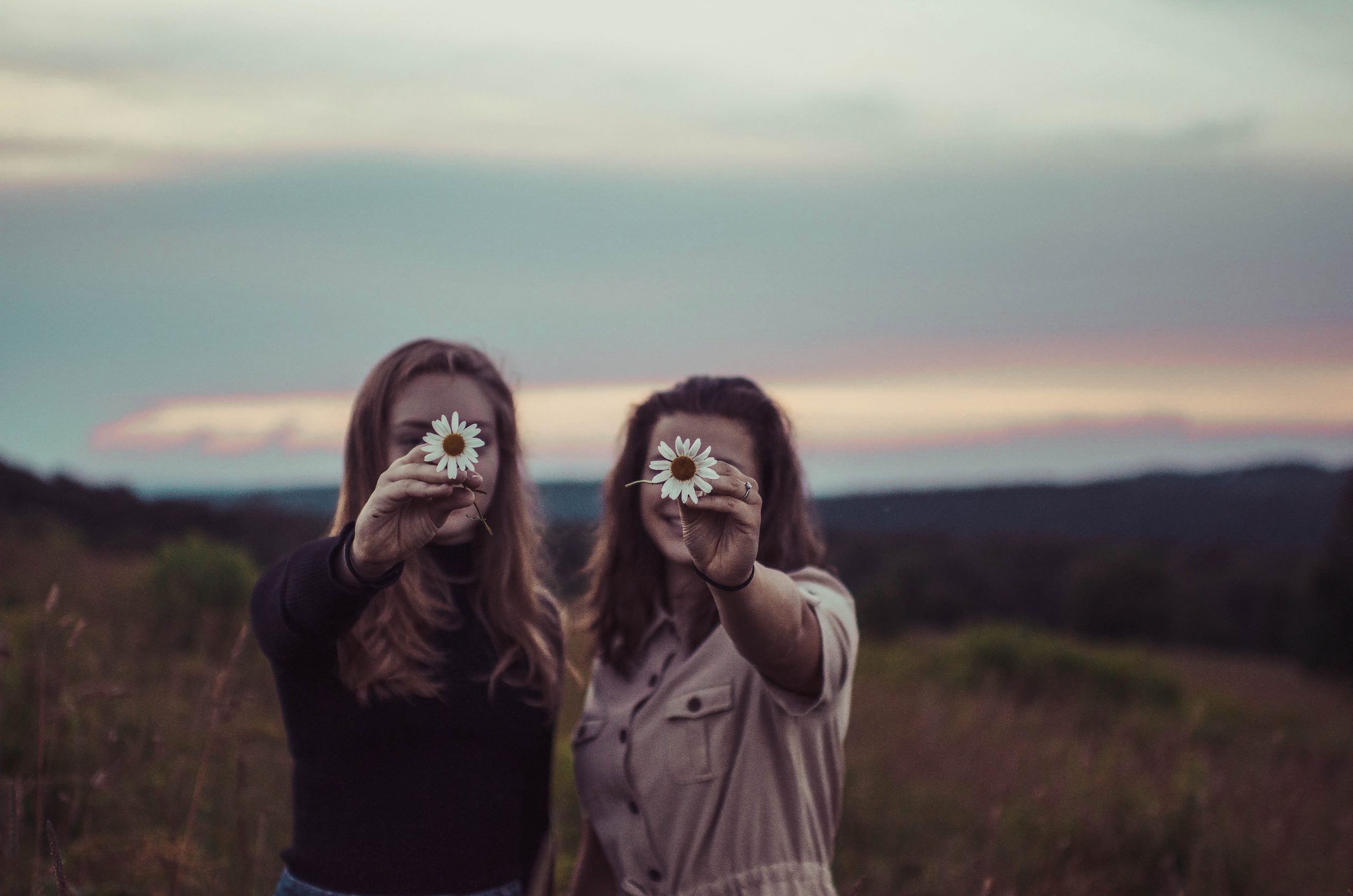 Two friends holding up wildflowers in front of their faces.
