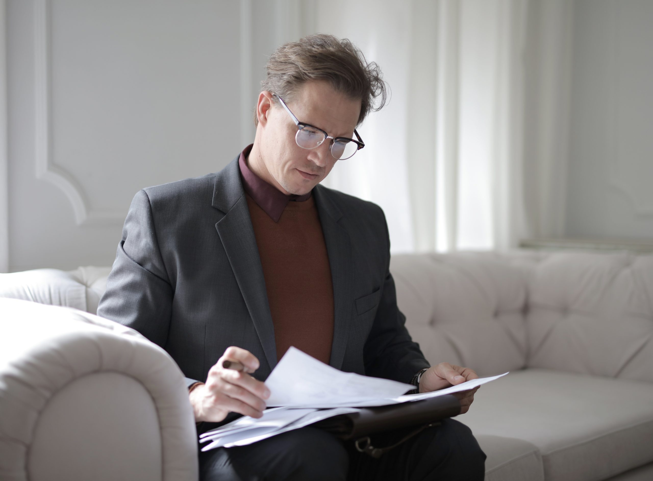 A man seated on a couch, looking through papers.