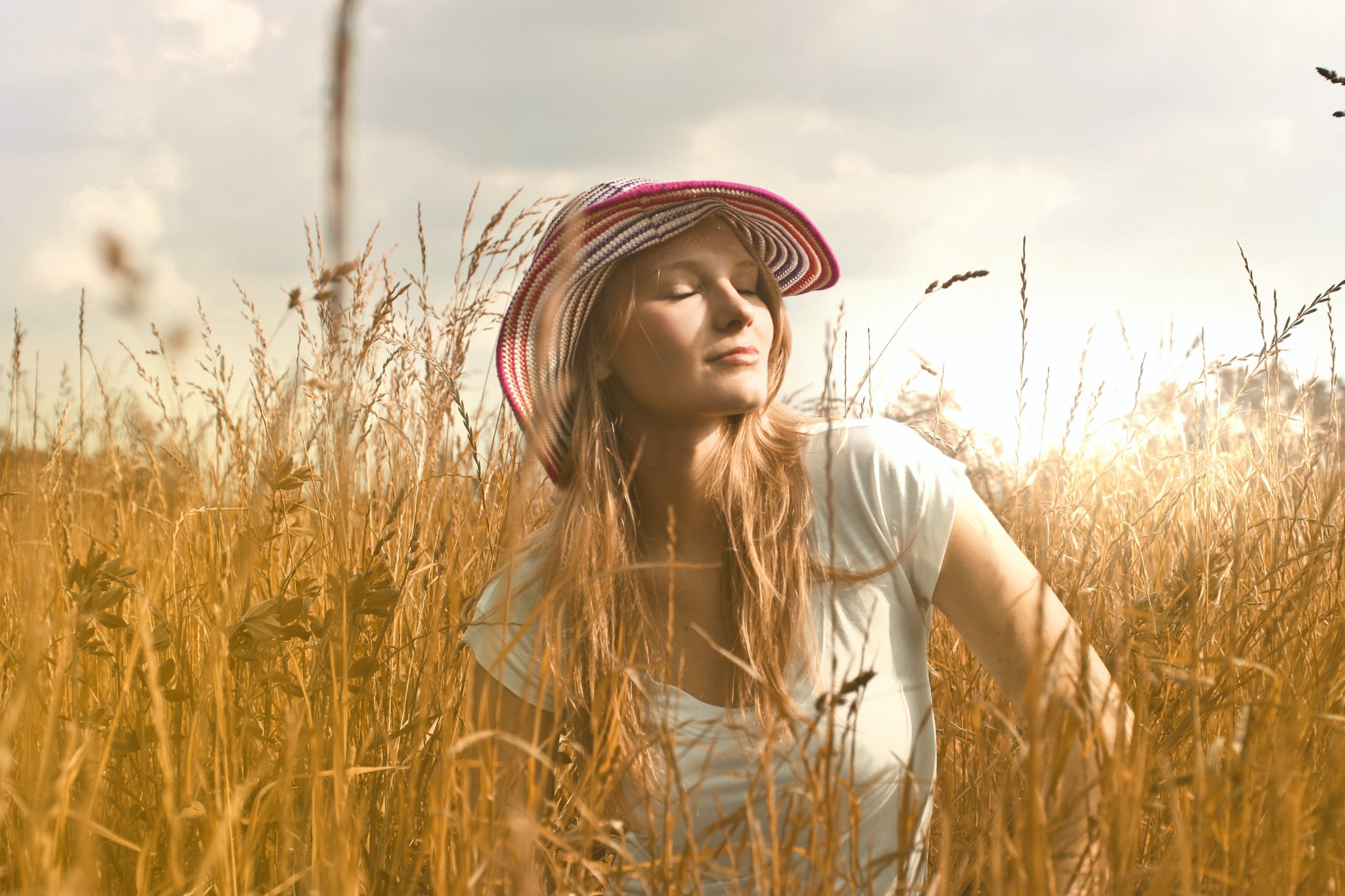 A woman standing in a grain field, her eyes closed in the sun.