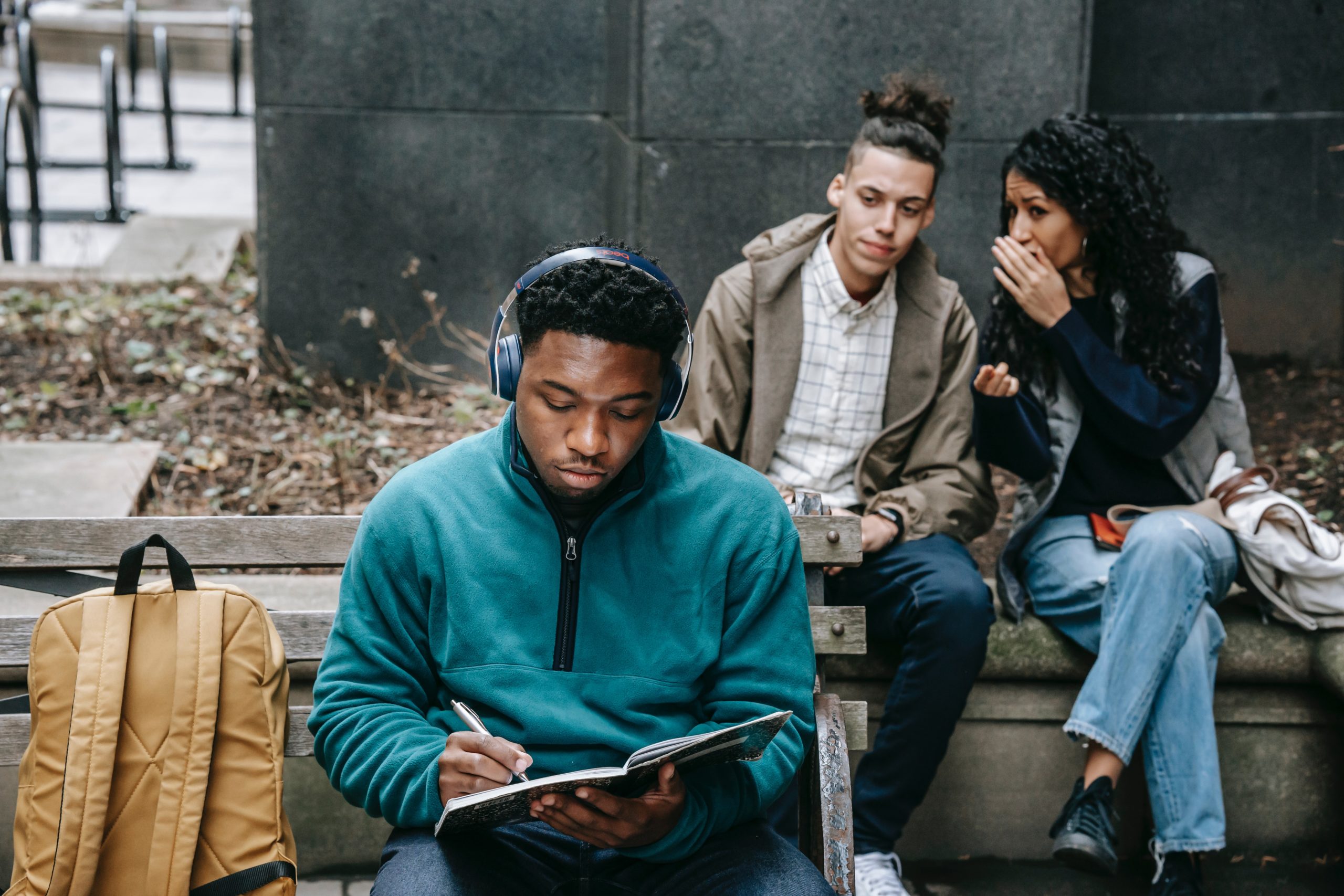 Two young people whispering about a third that's sitting in front of them.