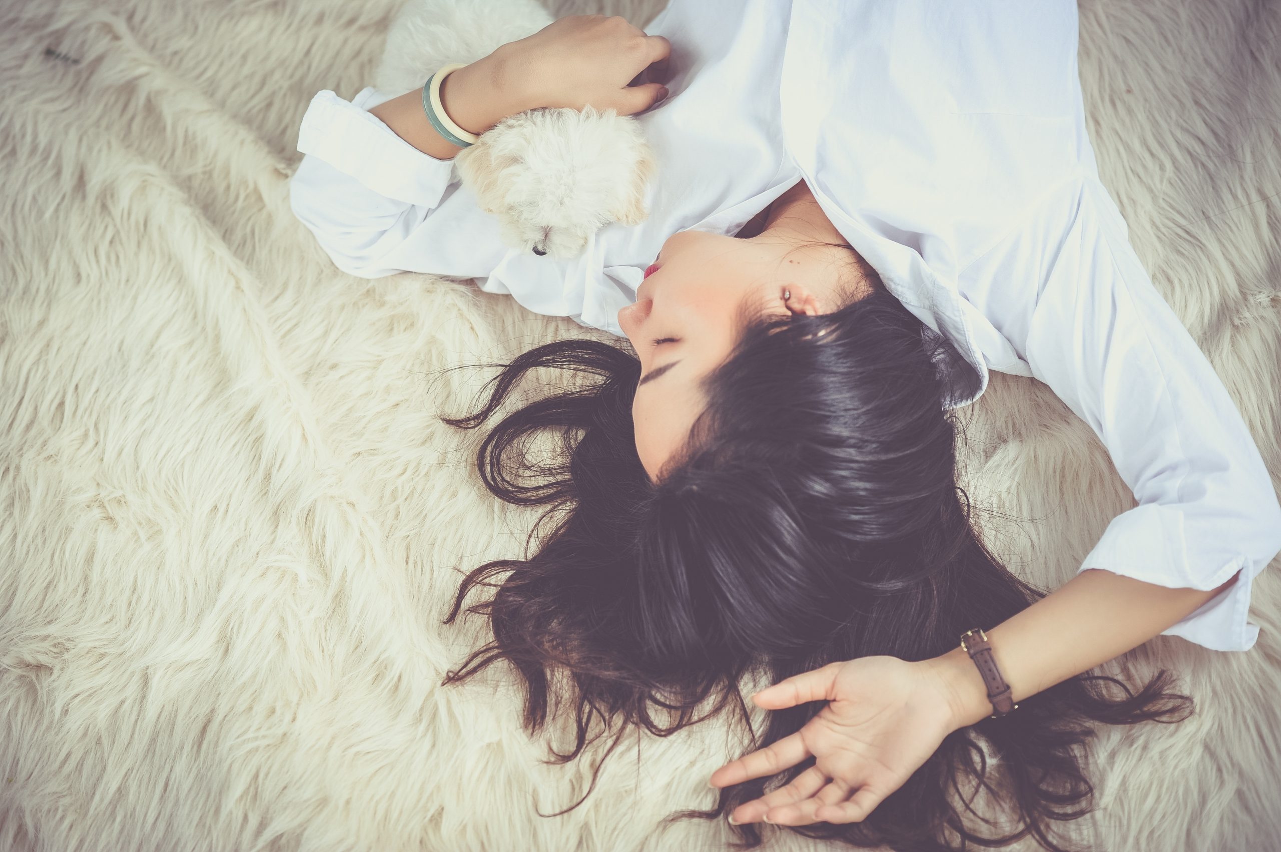 A woman laying on a soft, white blanket with her small dog.