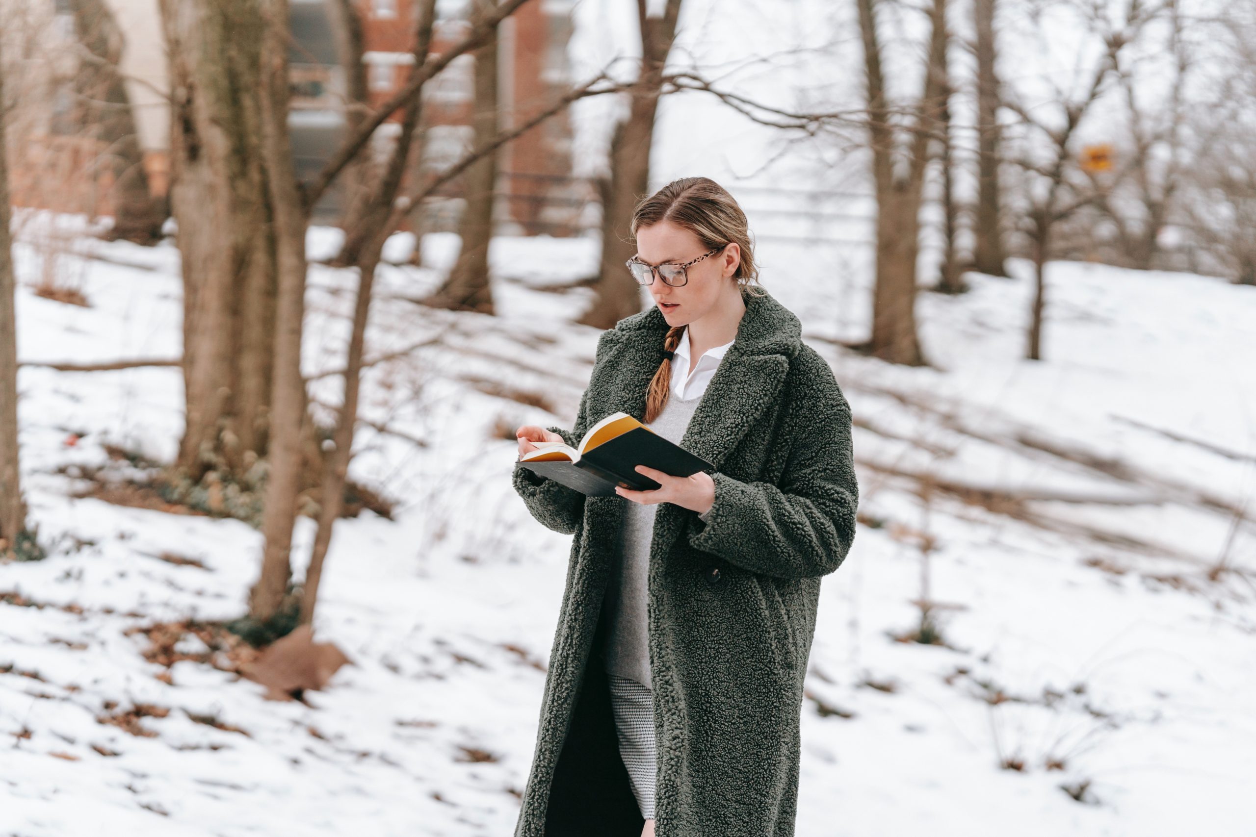 A woman standing in a snow-covered forest, reading a book.