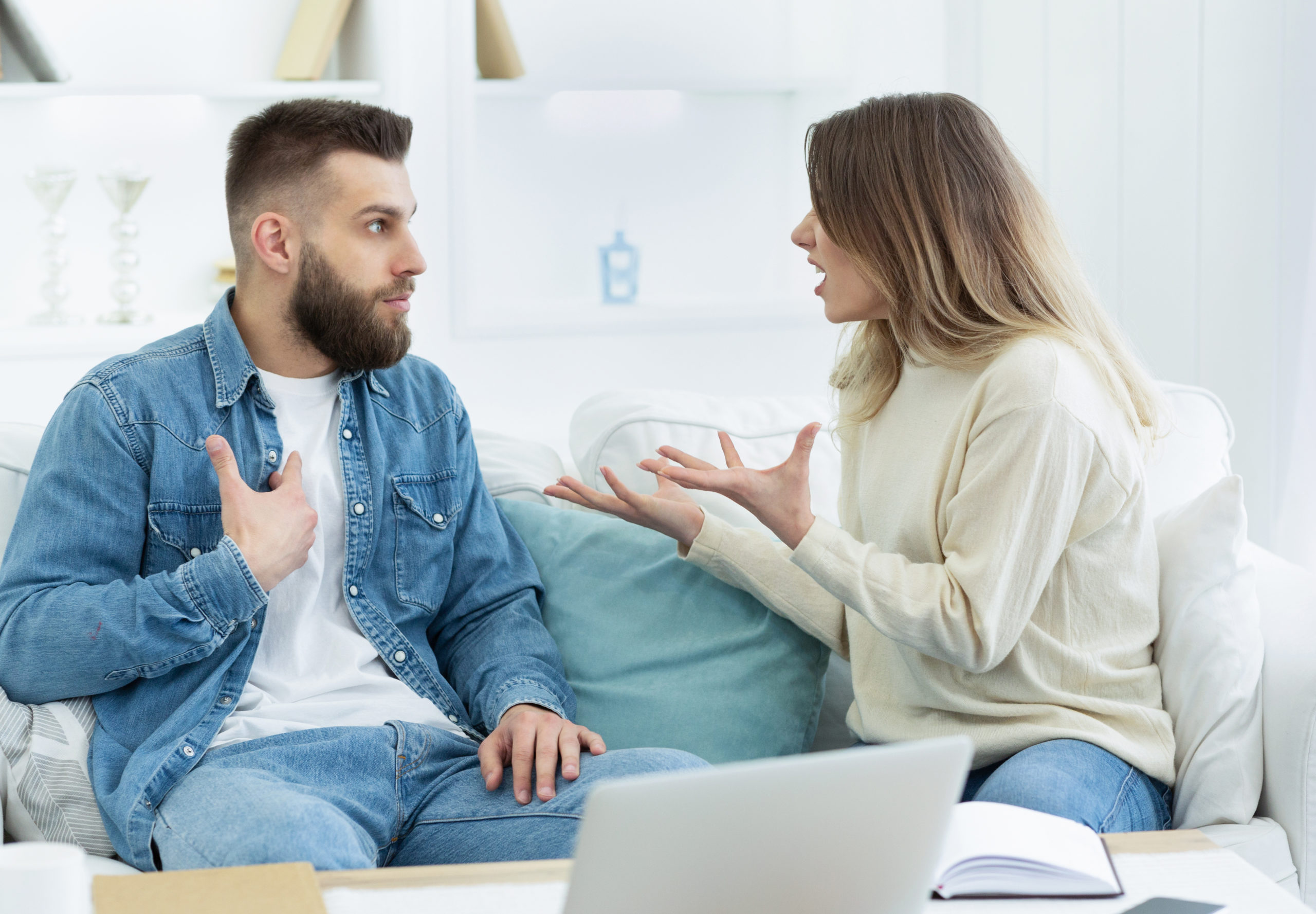man in denim shirt arguing on couch with woman in white