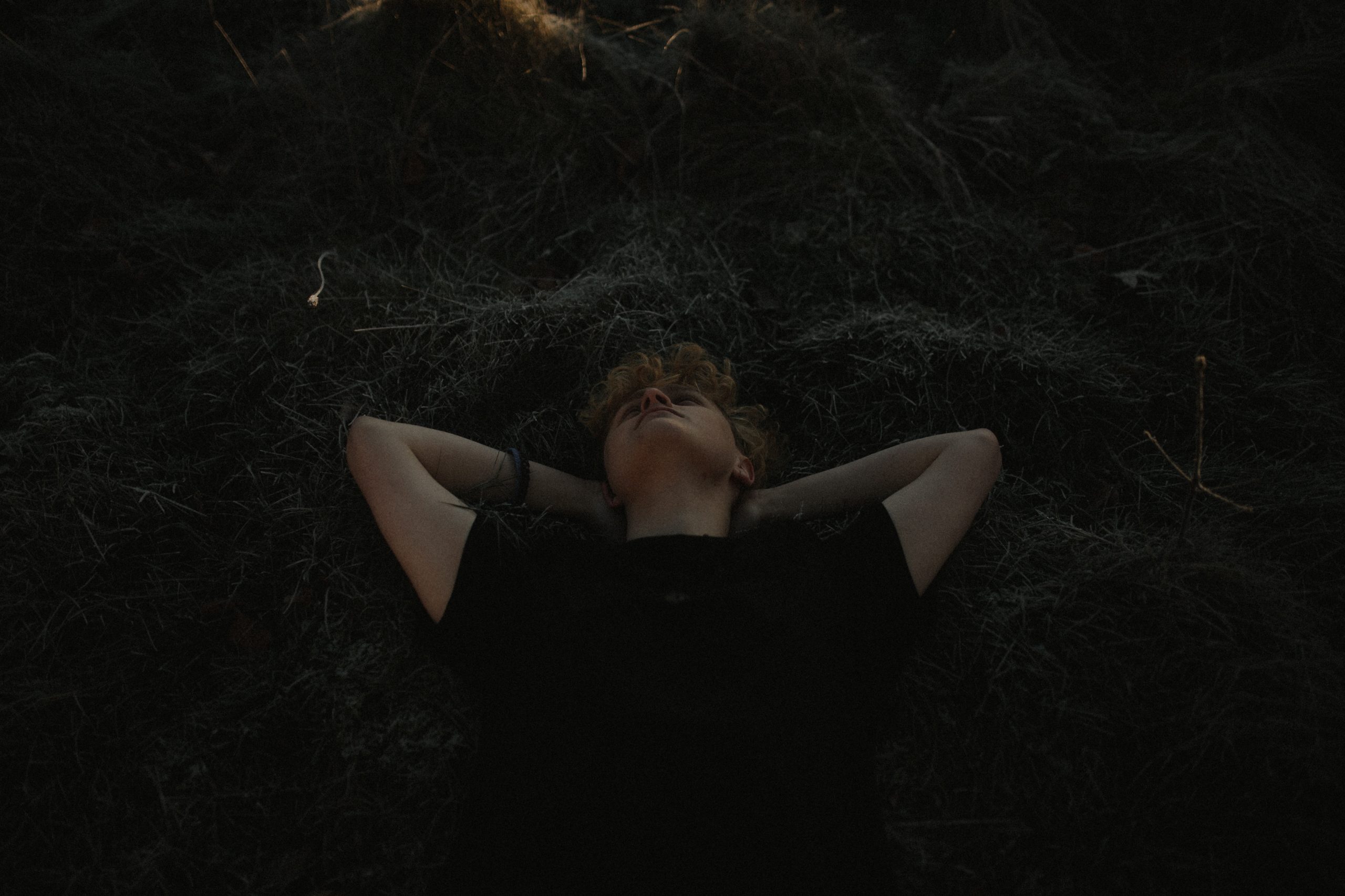 A boy laying in a field of dark crass, hands behind his head.