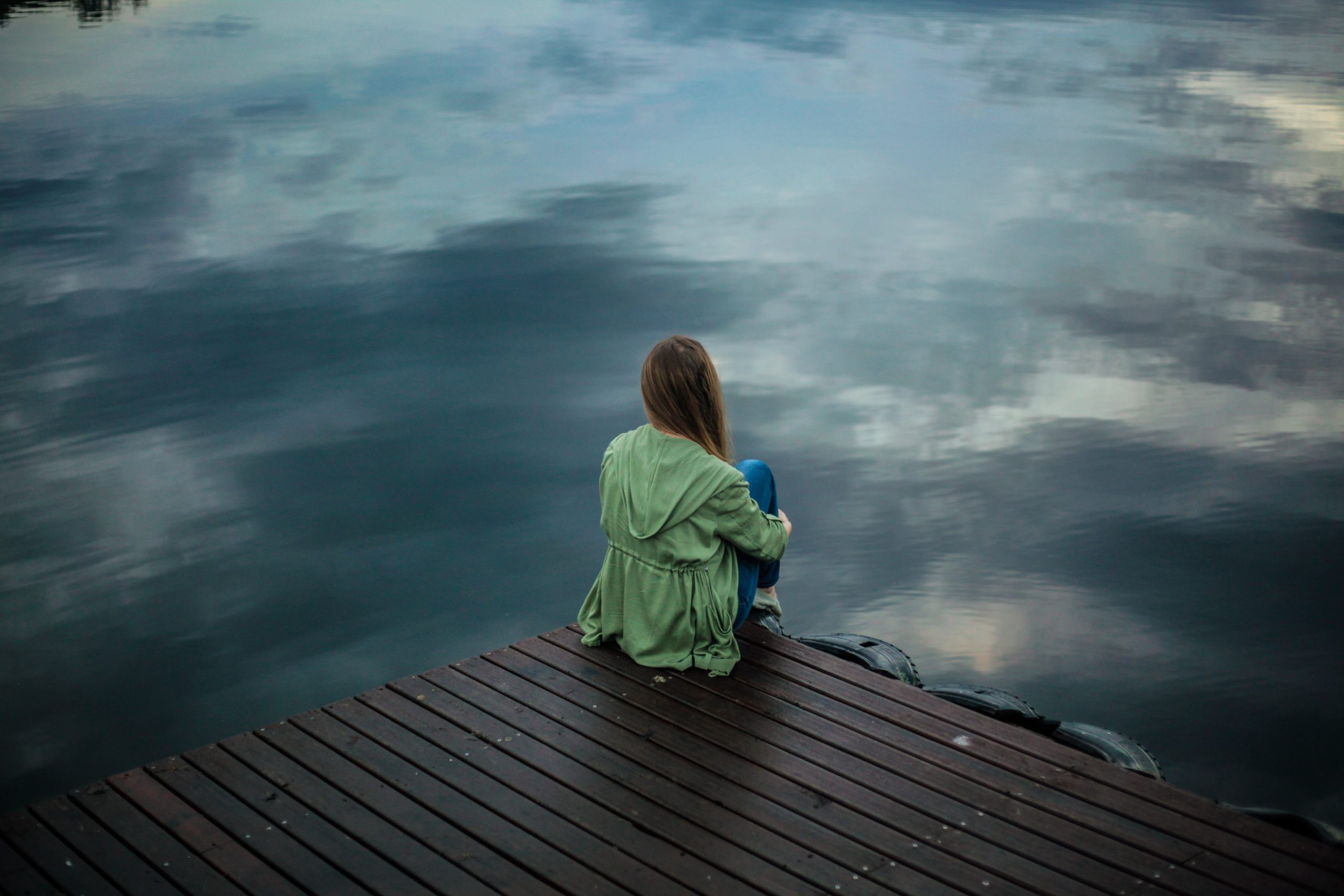 A woman sitting alone on a dock, looking out at the water.