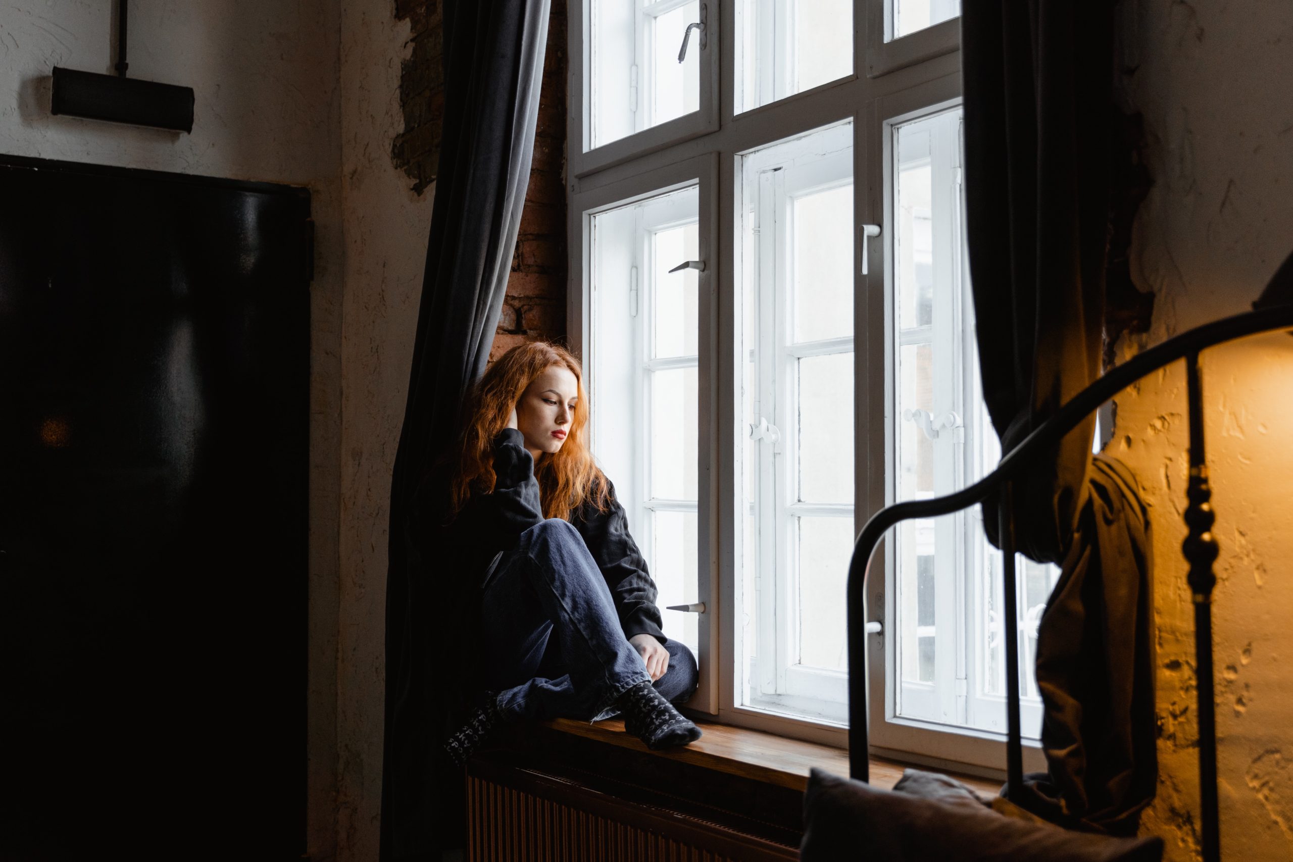 A woman sitting on a windowsill, looking outwards.