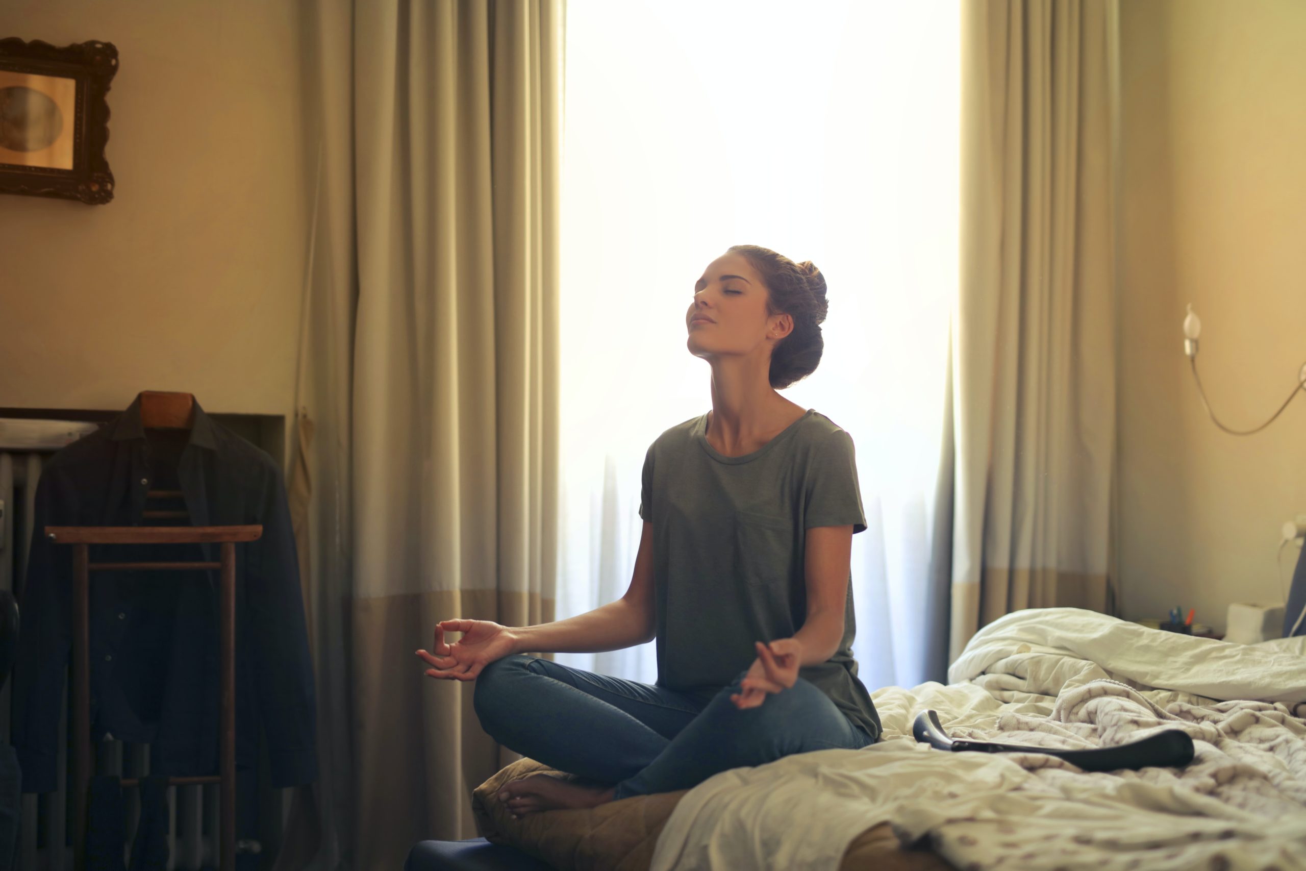 A woman meditating while sitting on the corner of her bed.