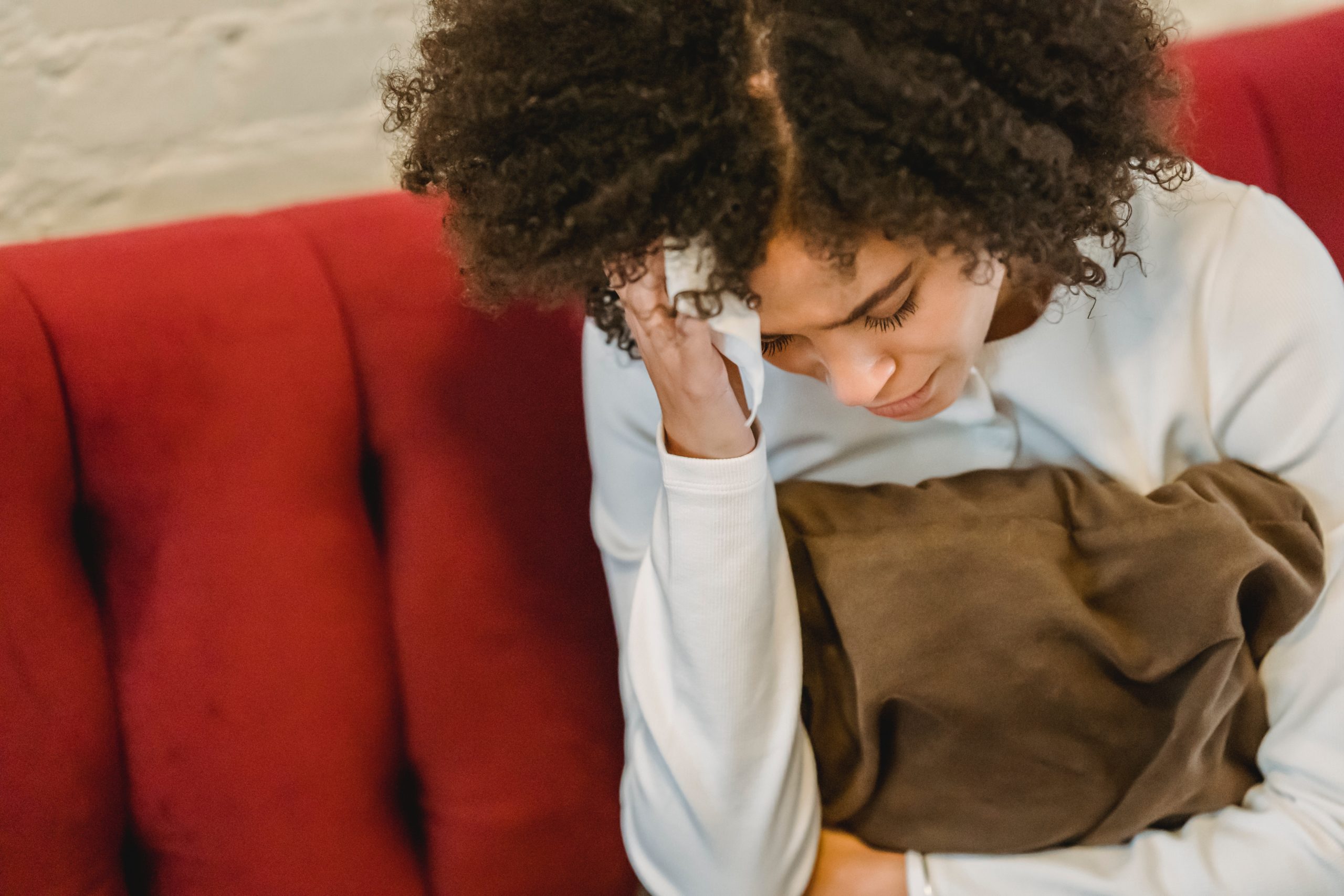 A woman sitting on a couch, hand to her head in discomfort.