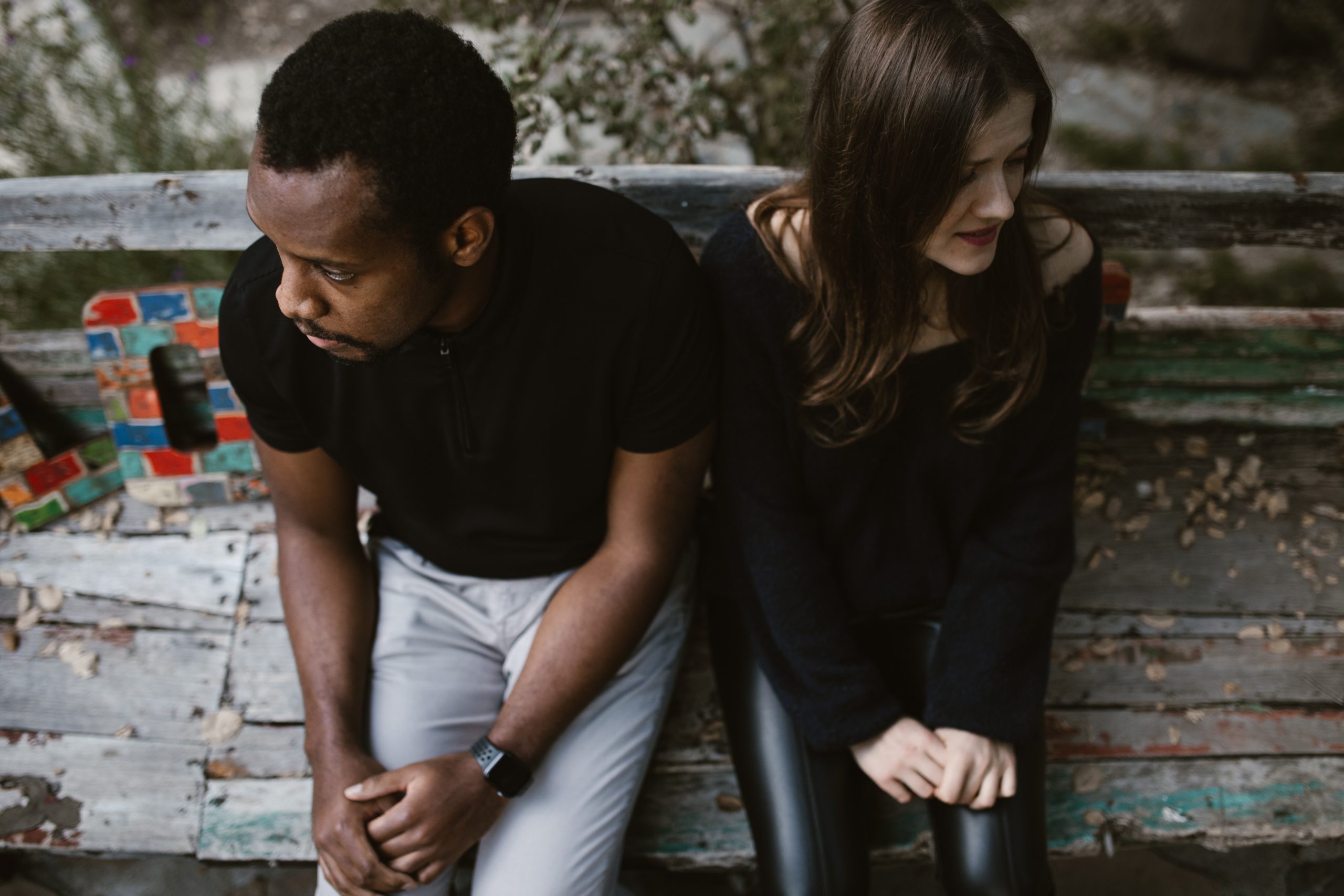 man and woman wearing dark clothing seated on wooden bench looking in opposite direction