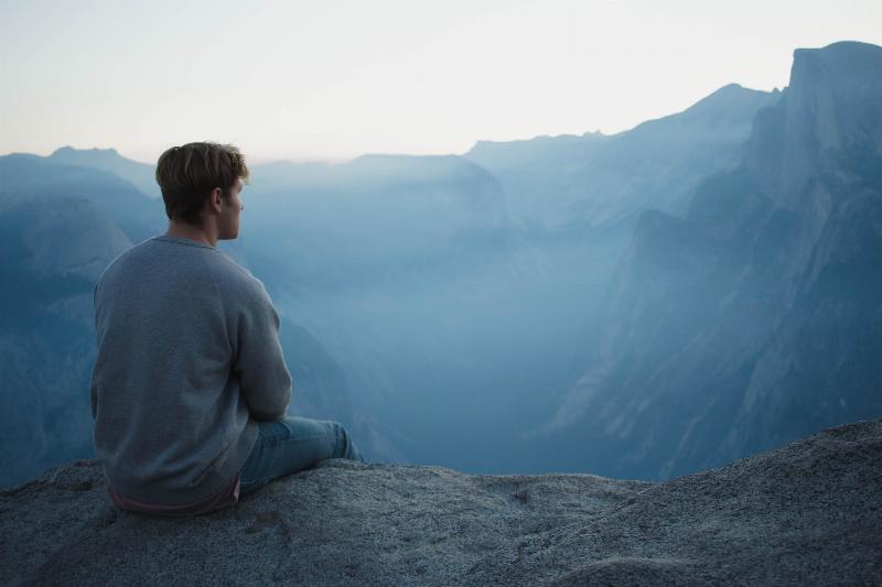 man sitting off a cliff looking into the distance