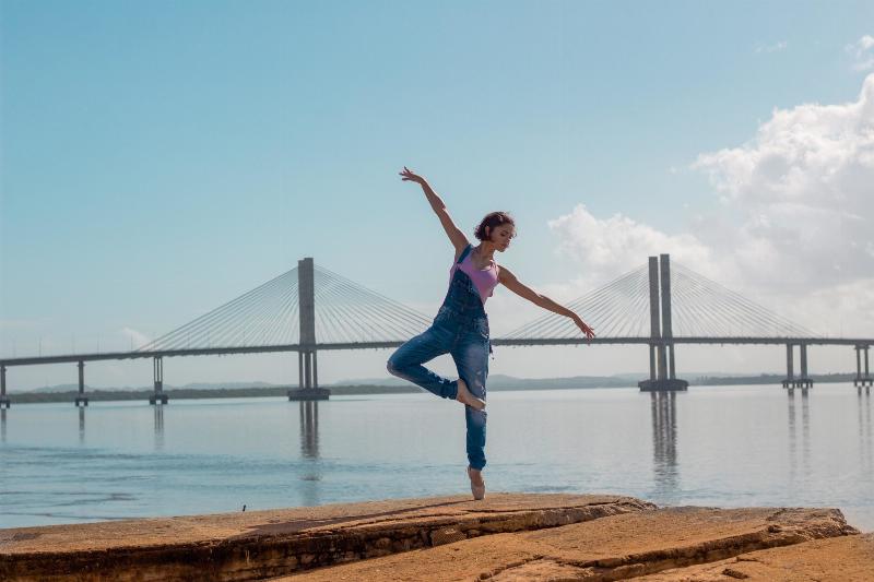ballerina en pointe in front of a bridge on the water