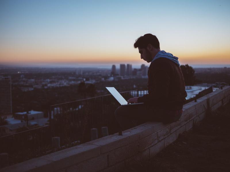 man typing on his laptop on a bridge