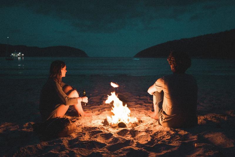 couple sits round campfire on the beach