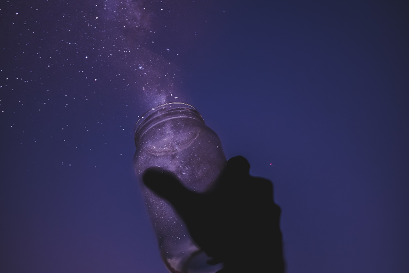 hand holding jar and releasing its magic into the purple sky