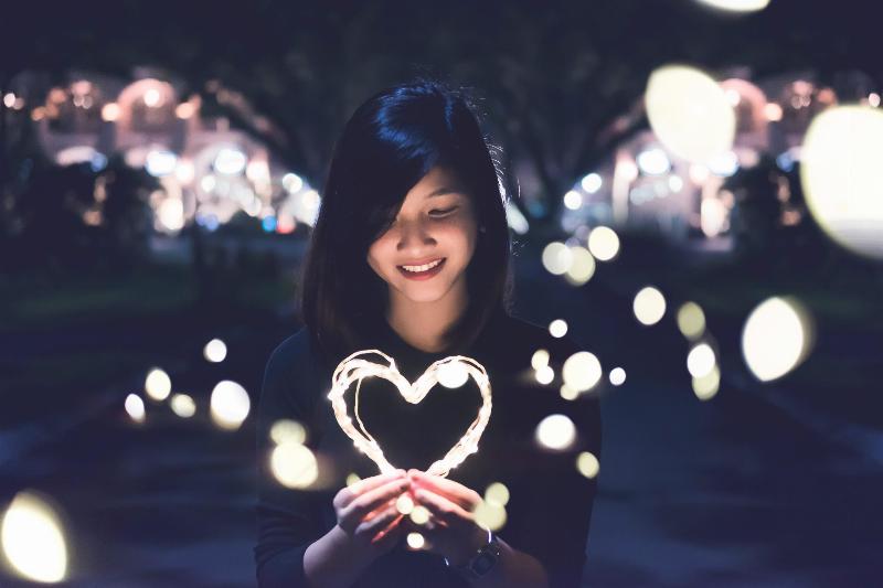 woman holding string light in the shape of a heart and smiling