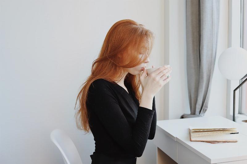 woman sipping on coffee mug at her desk with a journal