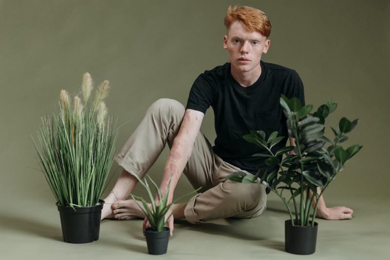 man sits in front of three plants barefoot