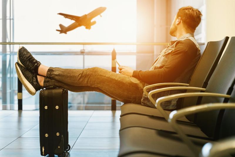 man at airport with his legs resting on suitcase, looking at plane taking off