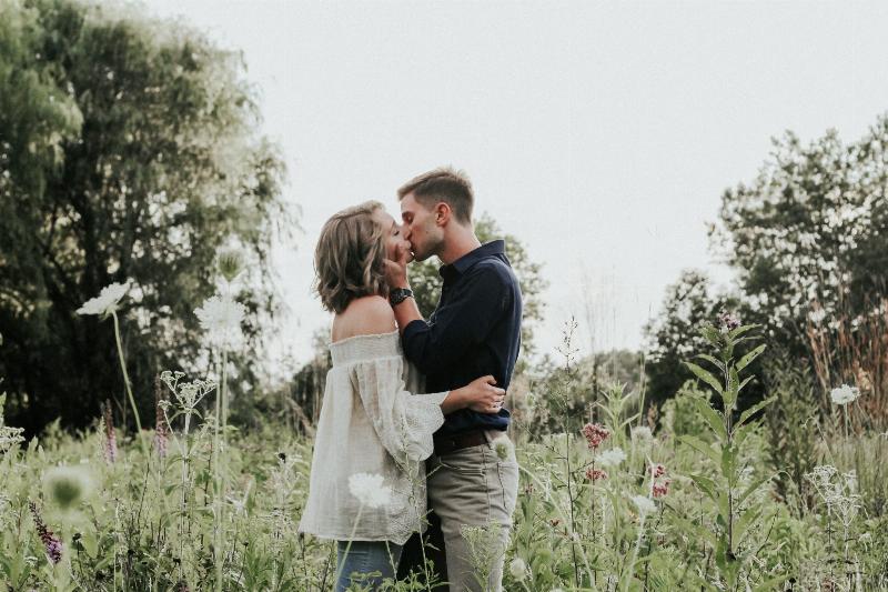 man and woman kissing while standing in a field
