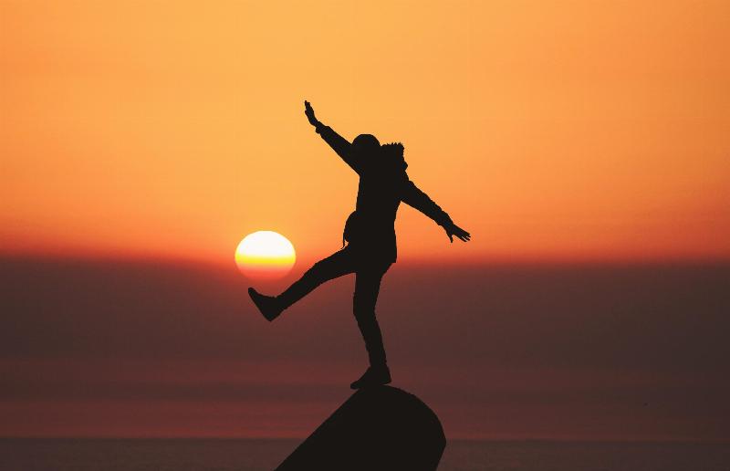 silhouette of a person balancing on a rock durinh sunrise