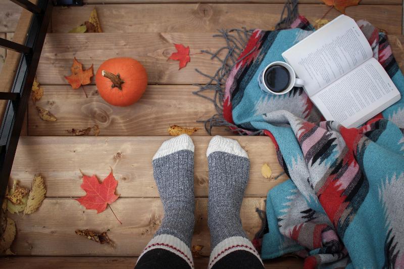 feet with socks on standing on staircase with a pumpkin, coffee, a book, a blanket and spread out fall leaves
