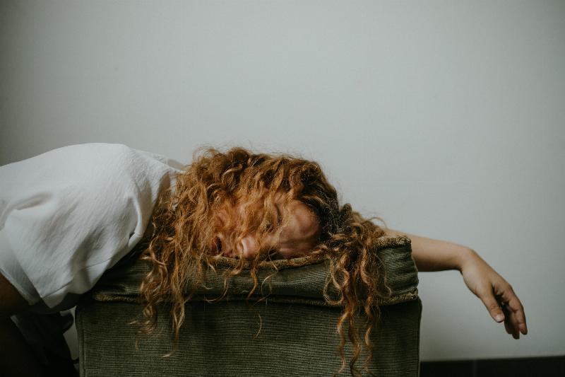 tired woman laying on cushion with her arm hanging off and her hair above her face