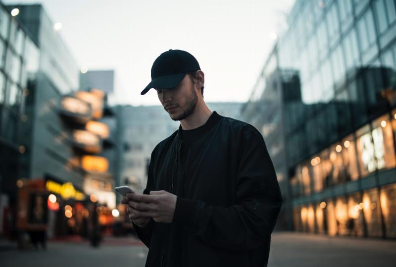 man looking down at phone and texting by building in the evening