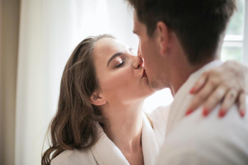 woman puts her hand around man's neck and kisses him while both are dressed in robes