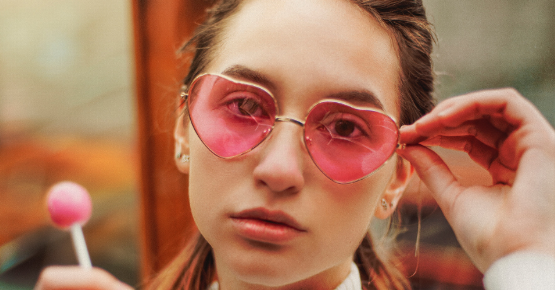 woman wearing heart shaped pink glasses and holding pink lollipop