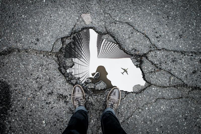 two feet stand by puddle water with reflection of person and plane