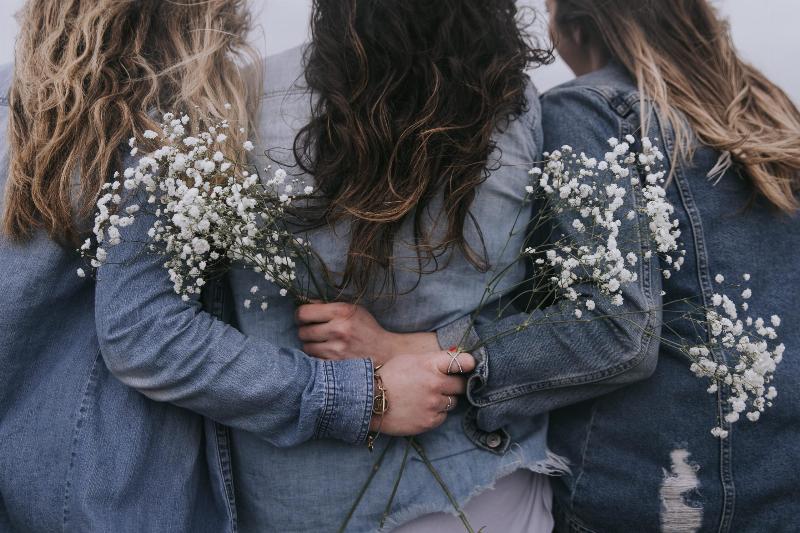 three women link arms from the back wearing denim jackets