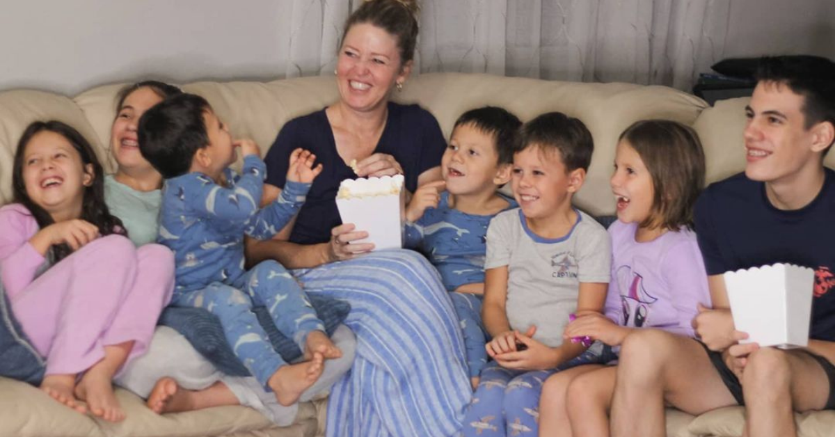 pam and 7 kids watching movie and laughing on couch with popcorn