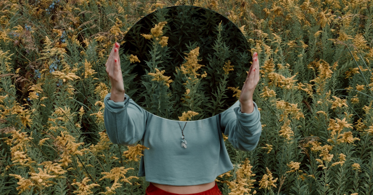 woman holding up mirror reflecting field