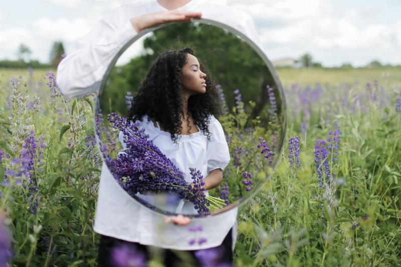 person holding up mirror reflecting woman holding lavender