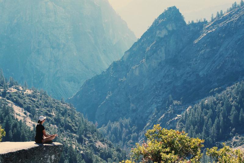 woman meditates on top of cliff by mountains