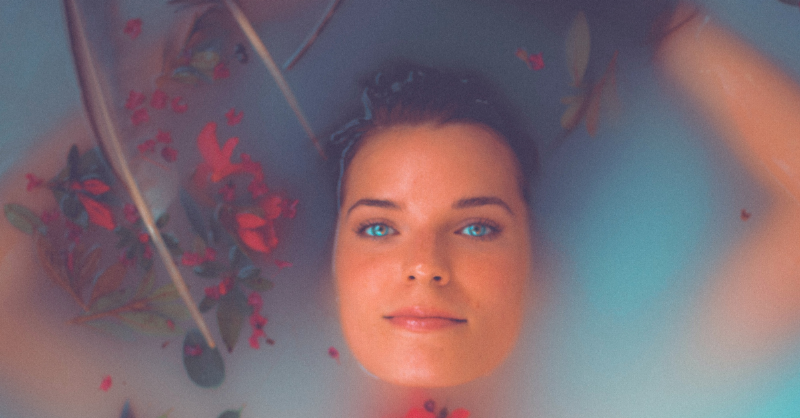 woman submerged under water in a bath with flowers around her