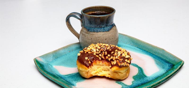 coffee and donut with a bite eaten o blue ceramic plate