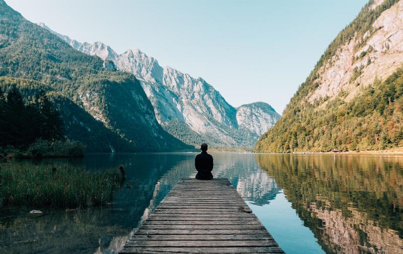 person sits on dock facing the mountains view