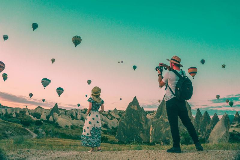 man taking picture of woman looking up at air balloons