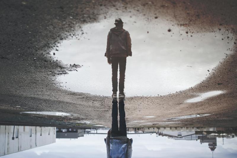 man stands above water reflection on street