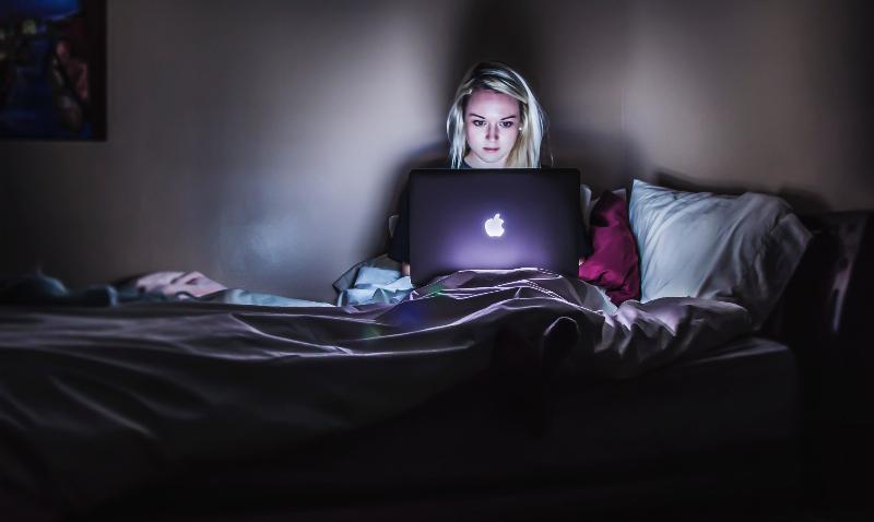 woman typing on apple laptop in the dark in bed